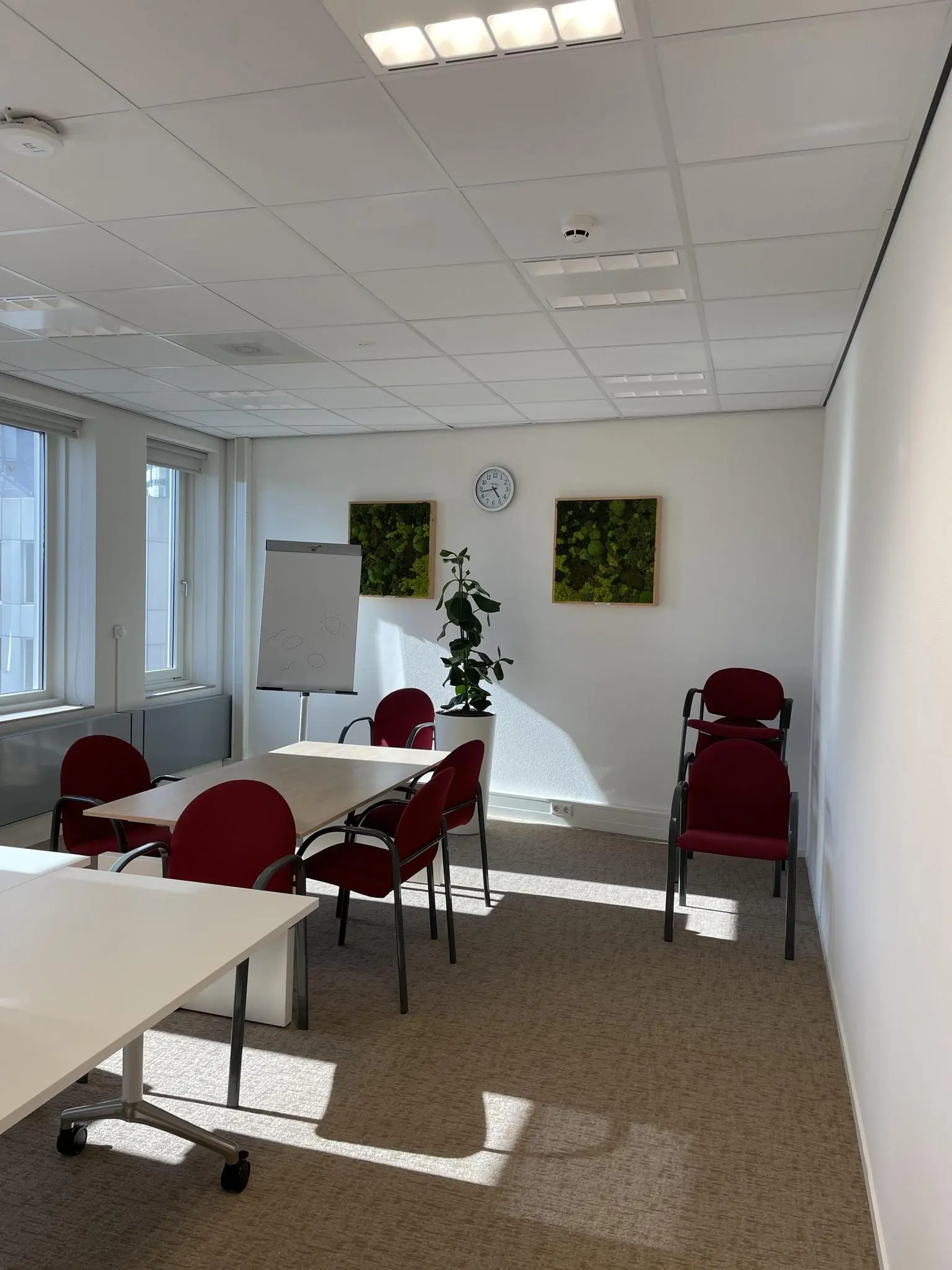 Vergaderruimte op de Johan Cruijff Boulevard met rode stoelen, een flip-over, wandklok en groene wanddecoratie.